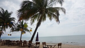A beach with wooden tables and chairs under palm trees, overlooking the sea. - Anandah Beach Resort (Takua Pa)