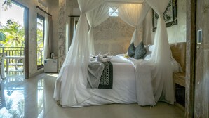 A spacious bedroom with a canopy bed, a small bedside table, and a view of palm trees through a large window.