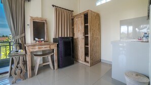 A room with a wooden desk, a wardrobe, a refrigerator, a sink, and a window with curtains.