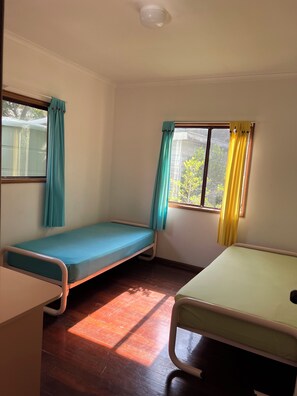 A room with two single beds, a window with curtains, and a ceiling light fixture.