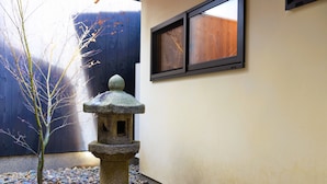 A stone lantern in a courtyard with a wooden fence and a window in the background. - Chika Rakuen (Kyoto)