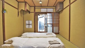 A traditional Japanese-style room with tatami flooring, two beds with white bedding, a shoji screen door, and a view of the outside. - Chika Rakuen (Kyoto)