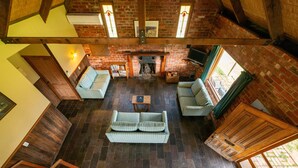 A spacious living room with a fireplace, wooden floors, and a high ceiling. - Grampians Pioneer stone cabin (Halls Gap)