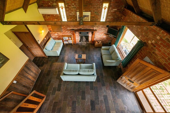 A spacious living room with a fireplace, wooden floors, and a high ceiling.