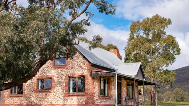 A stone house with a porch, large windows, and a grassy yard. - Grampians Pioneer stone cabin (Halls Gap)