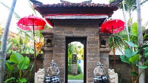 Une arche en pierre de style traditionnel, flanquée de deux statues de chaque côté, chacune tenant un bol. Des parasols rouges sont placés au-dessus de l’arche.