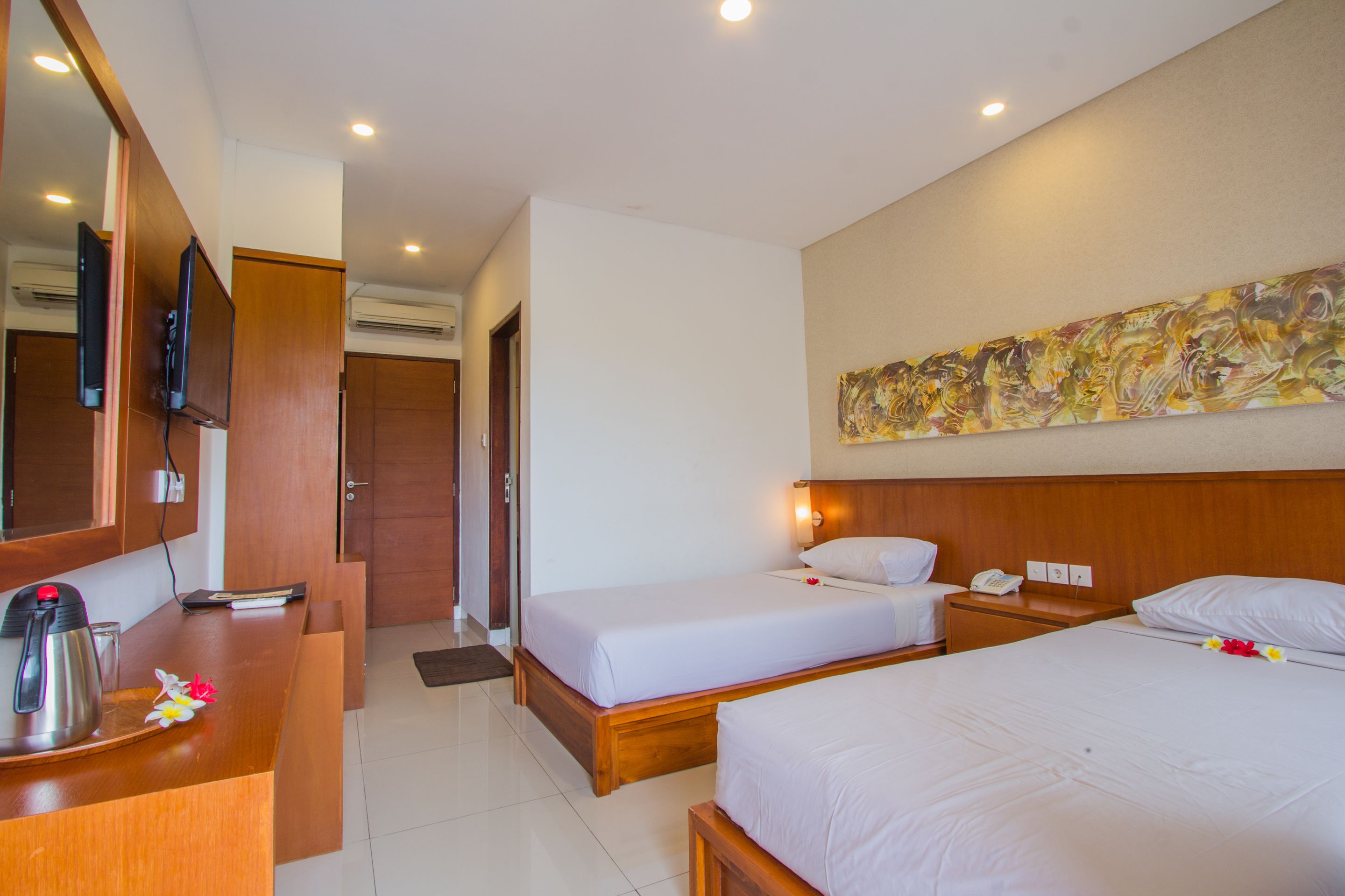 A hotel room with two beds, a wooden desk with a coffee maker, a telephone, and a painting on the wall.