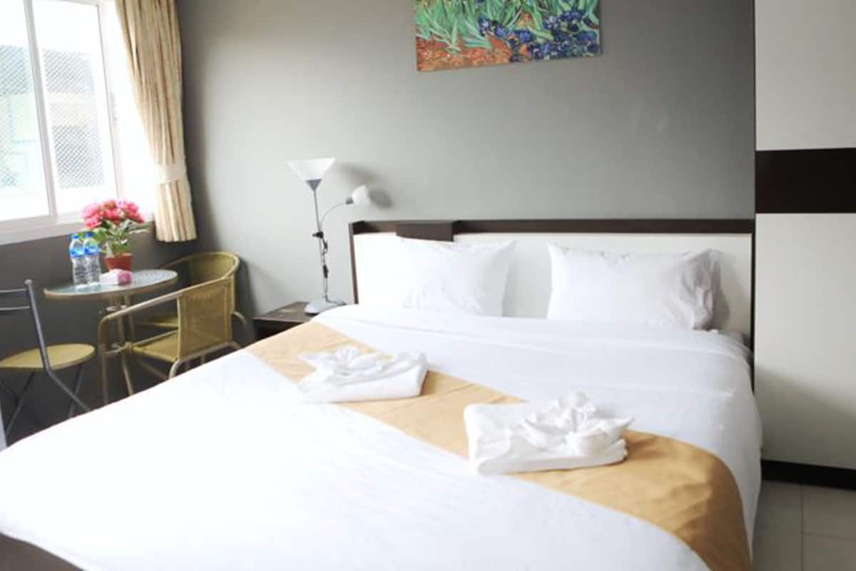 A hotel room with a bed, a desk, a chair, a lamp, and a painting on the wall.