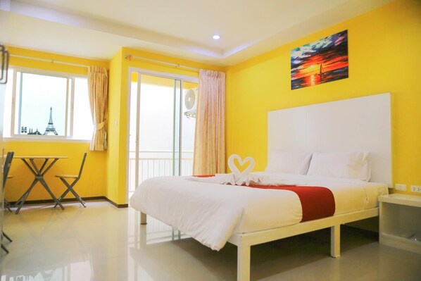 A hotel room with a bed, a window with a view of the Eiffel Tower, a balcony with a fan, and a table with chairs. - Guan Chao Yin Hotel (Patong)