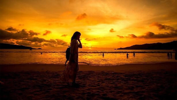Une scène de plage au coucher du soleil, avec des silhouettes de personnes et un bateau.