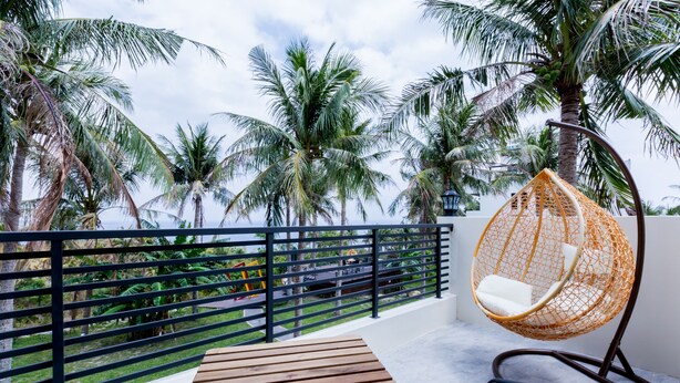 A balcony with a wooden table and a hanging chair, surrounded by palm trees and a view of the sea. - Rich Sunshine Inn (Beinan)