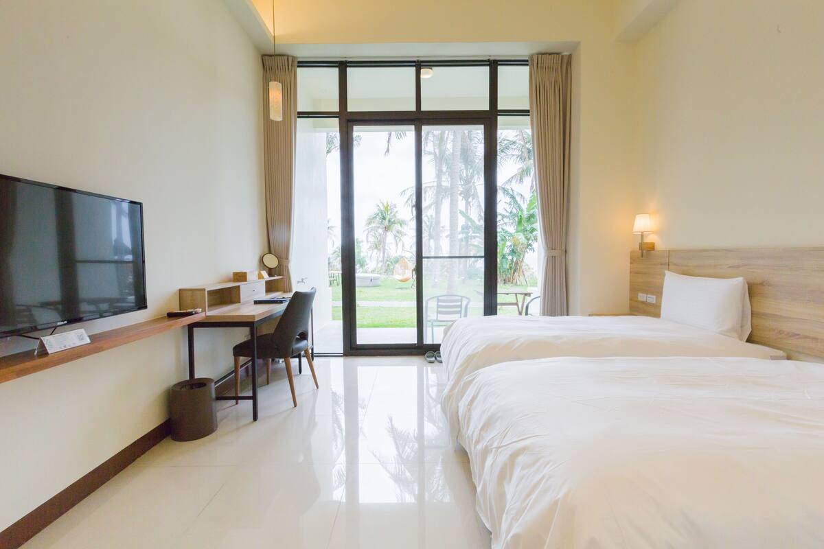 A hotel room with a bed, a desk with a chair, a television, and a view of the outdoors through a glass door.