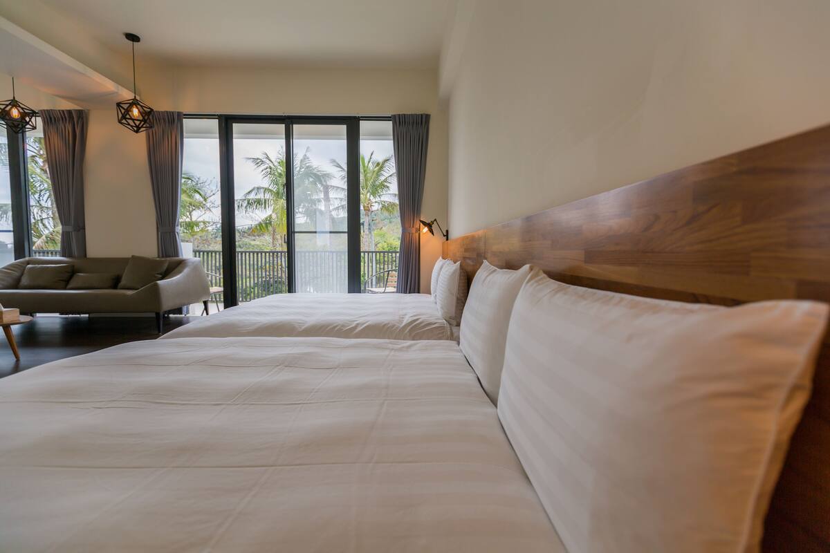 A hotel room with a large bed, a sofa, and a view of palm trees through the windows.