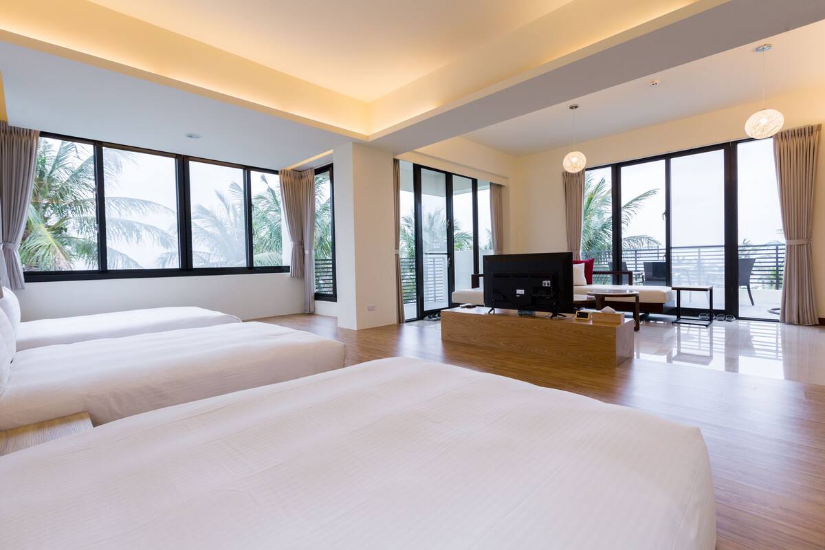 A modern hotel room with large windows, a flat-screen TV, a sofa, and a wooden coffee table.