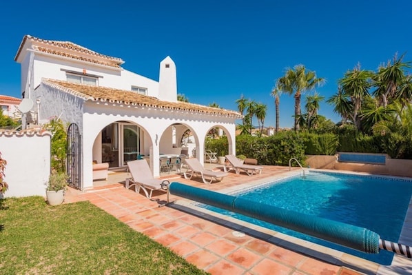 Una villa blanca con piscina, mobiliario exterior y palmeras.