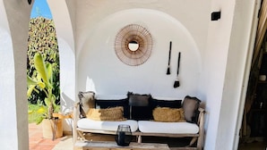 Eine gemütliche Terrasse mit einer Couch, zwei Stühlen, einem Wollteppich und einem wandmontierten Spiegel.