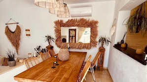 Ein geräumiger Essbereich mit einem großen Holztisch, Korbstühlen und hängenden Pendelleuchten.