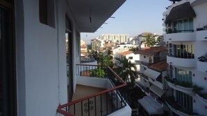 Un balcón con barandilla de metal, con vistas a una zona residencial con edificios y palmeras.