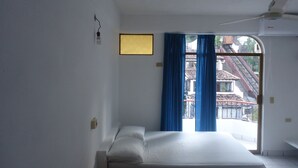 Un dormitorio con cama, ventilador de techo y ventana con cortinas azules.