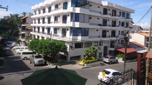 Un edificio blanco de varios pisos con balcones, un toldo verde y automóviles estacionados.
