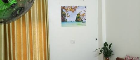 A hotel room with a bed, a nightstand, a wall-mounted air conditioner, a window with curtains, and a wall-mounted picture.