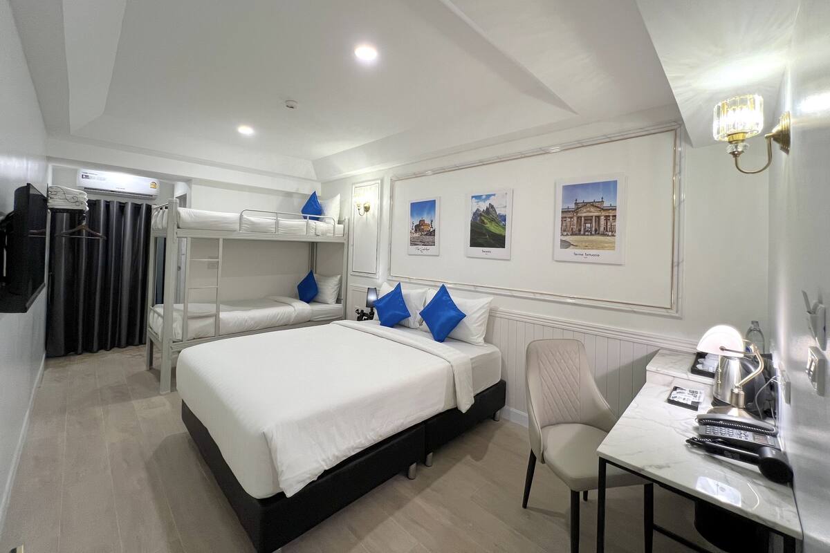 A hotel room with a large bed, a desk with a chair, a mirror, and a wall-mounted lamp.