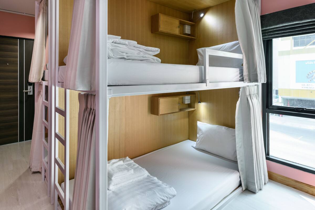 A bunk bed room with wooden walls, a window, and a small shelf.