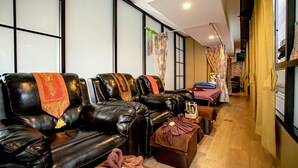 A room with leather sofas, a wooden floor, and a small table with a towel and flowers. - Travelier Hostel (Bangkok)