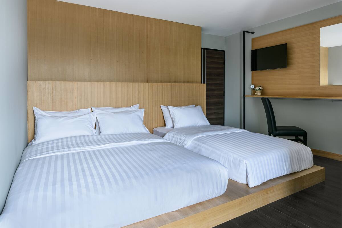 A modern hotel room with two beds, a mounted TV, and a wooden headboard.