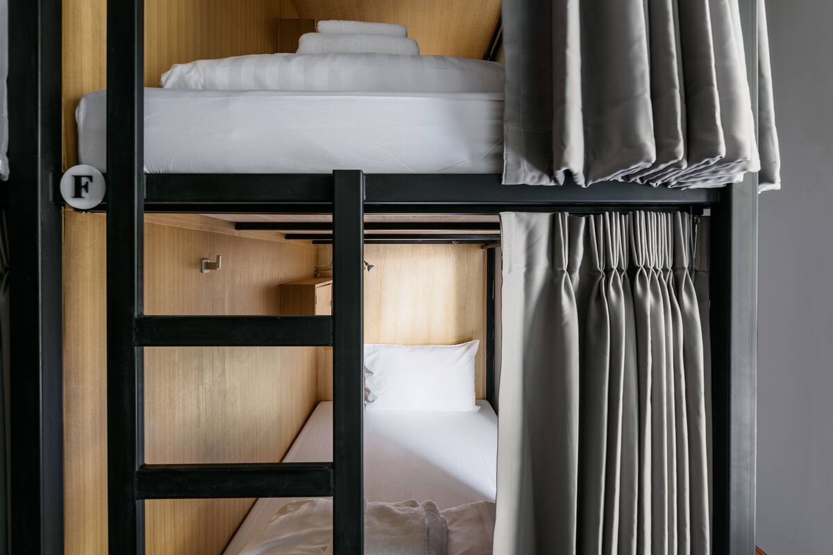 A bunk bed room with a wooden ladder, a pull-out desk, and a curtain.