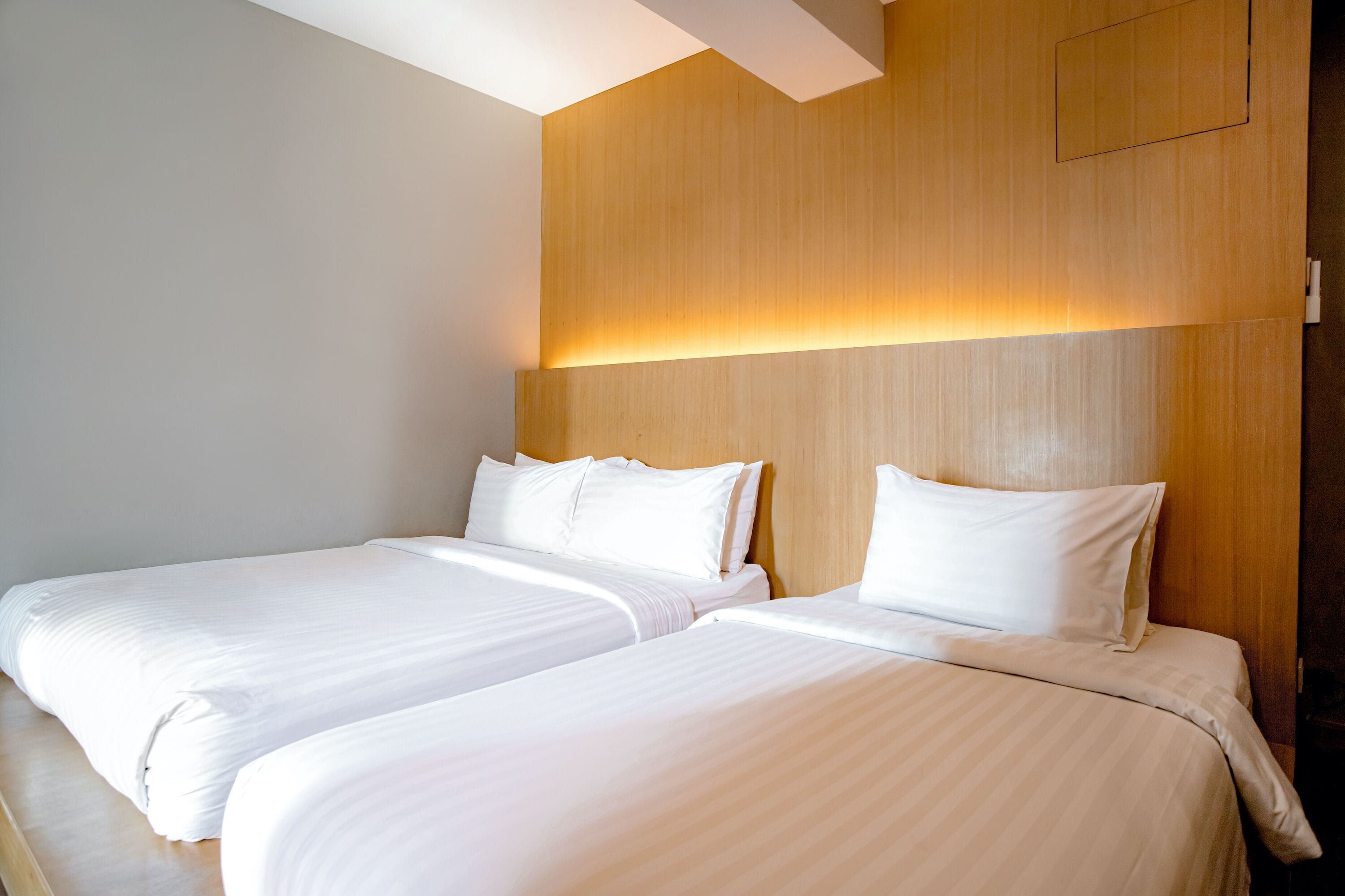 A hotel room with two beds, wooden headboard, and a wall-mounted light fixture.