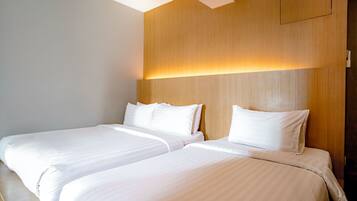 A hotel room with two beds, wooden headboard, and a wall-mounted light fixture.