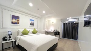 A hotel room with a large bed, a desk, a chair, a TV, and a wardrobe. - Travelier Hostel (Bangkok)