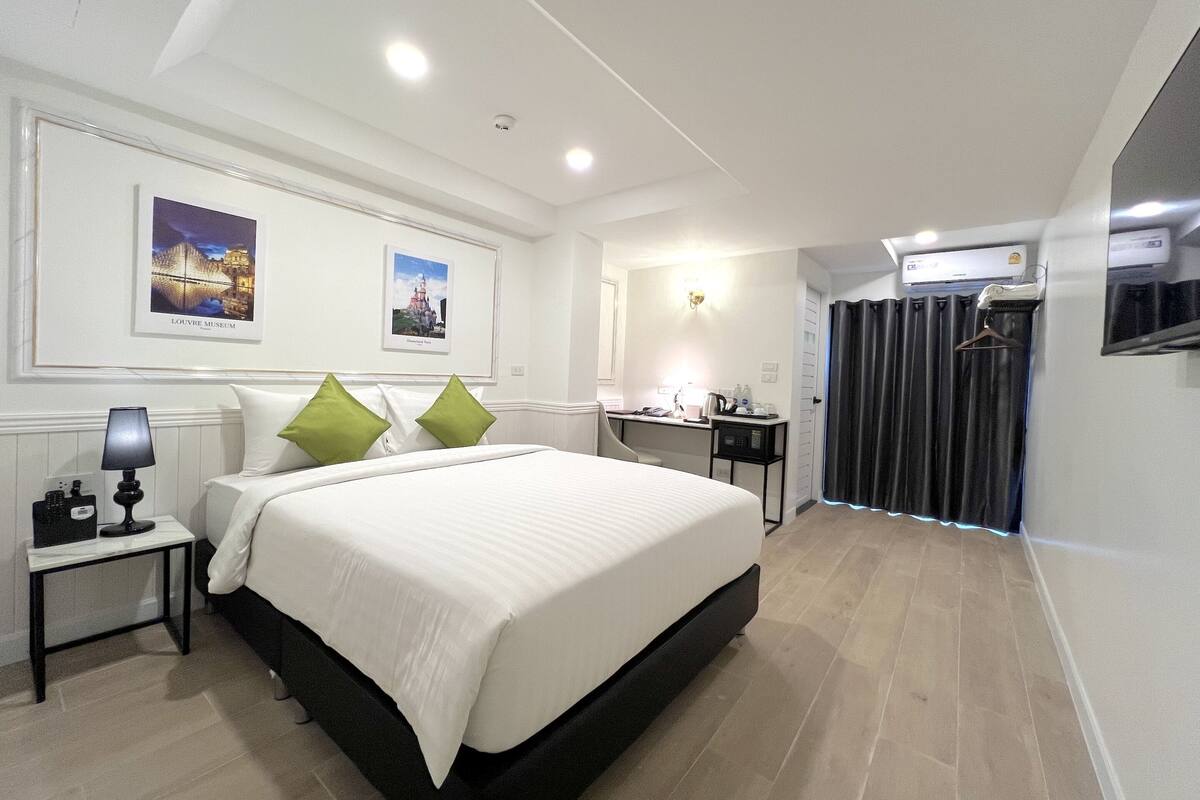 A hotel room with a large bed, a desk, a chair, a TV, and a wardrobe.
