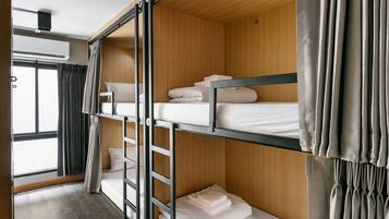 A bunk bed room with wooden paneling, a window with curtains, and a ceiling-mounted air conditioning unit.