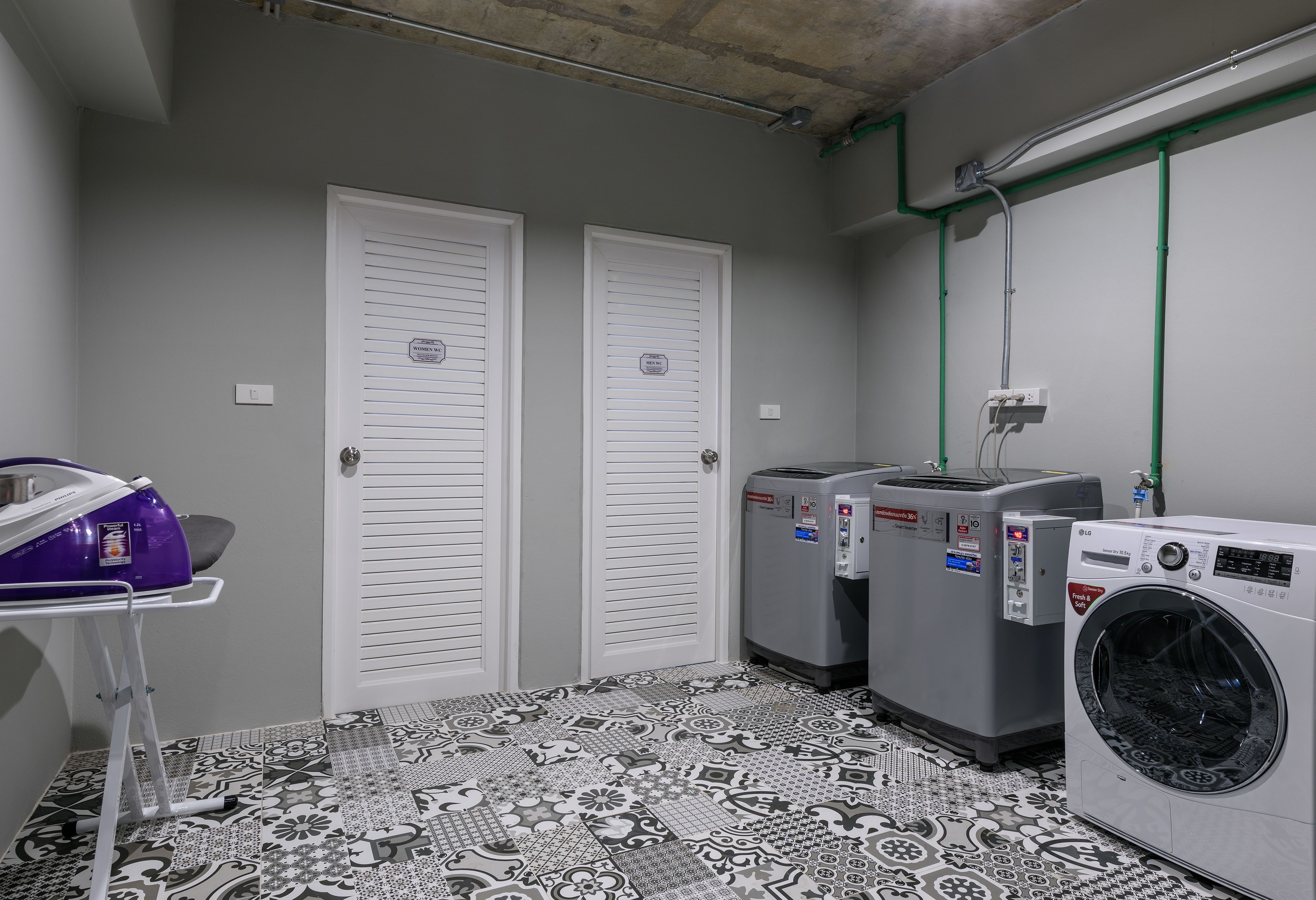 Une buanderie avec deux portes blanches, un lave-linge, un sèche-linge et un panier à linge violet posé sur un sol à motifs.