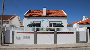 A white building with a red-tiled roof, a sign reading "Casa do Bairro by Coca-Cola," and a gated entrance with two green umbrellas. - Green Studio with private patio, 200 meters, 3 min by foot Beach of Peniche (Peniche)