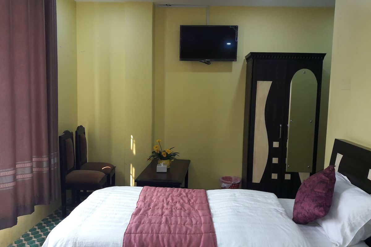 A hotel room with a bed, a television mounted on the wall, a mirror, and a desk with a vase of flowers.