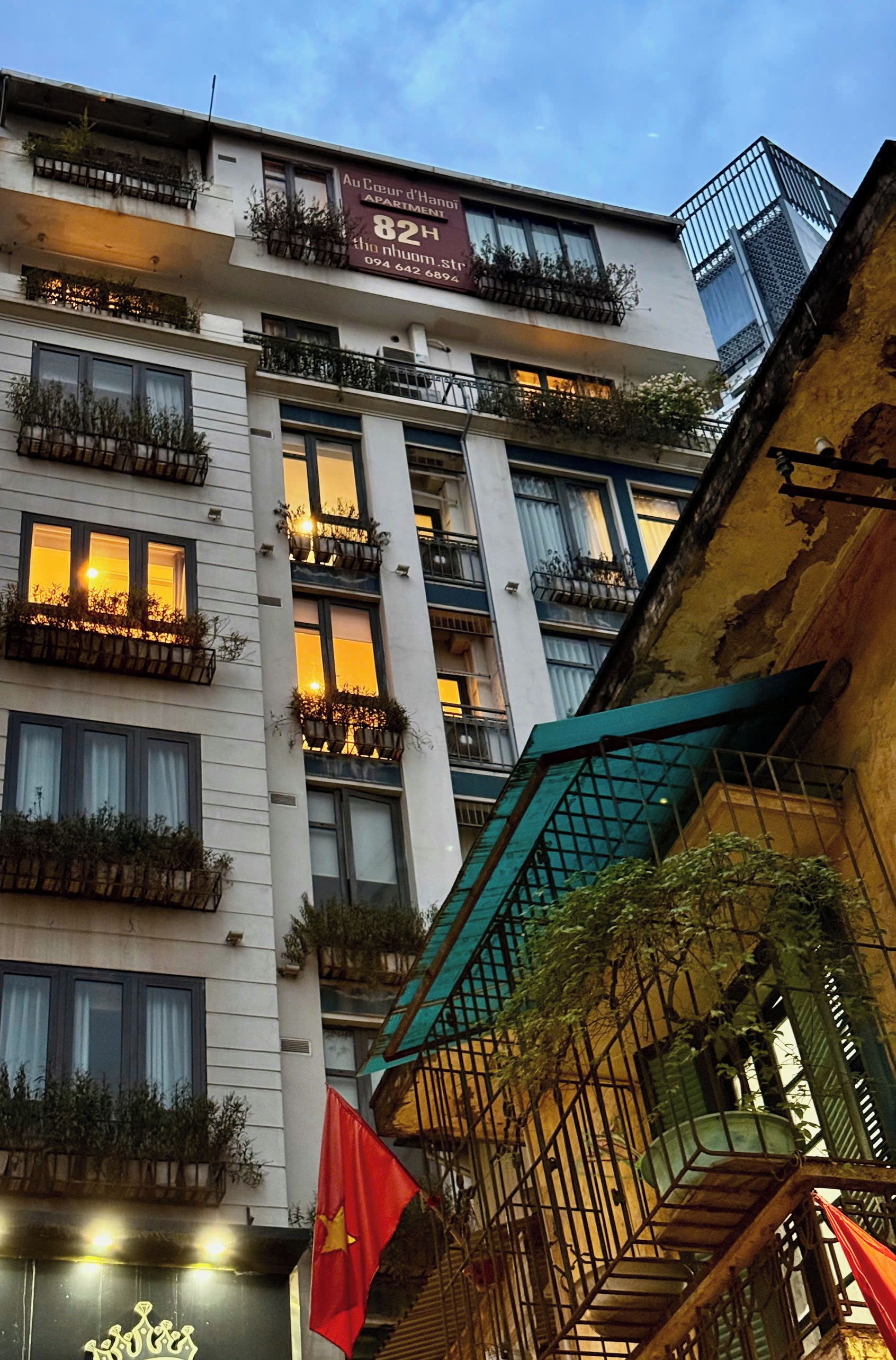 A multi-story building with balconies, a flag, and a sign indicating an apartment.