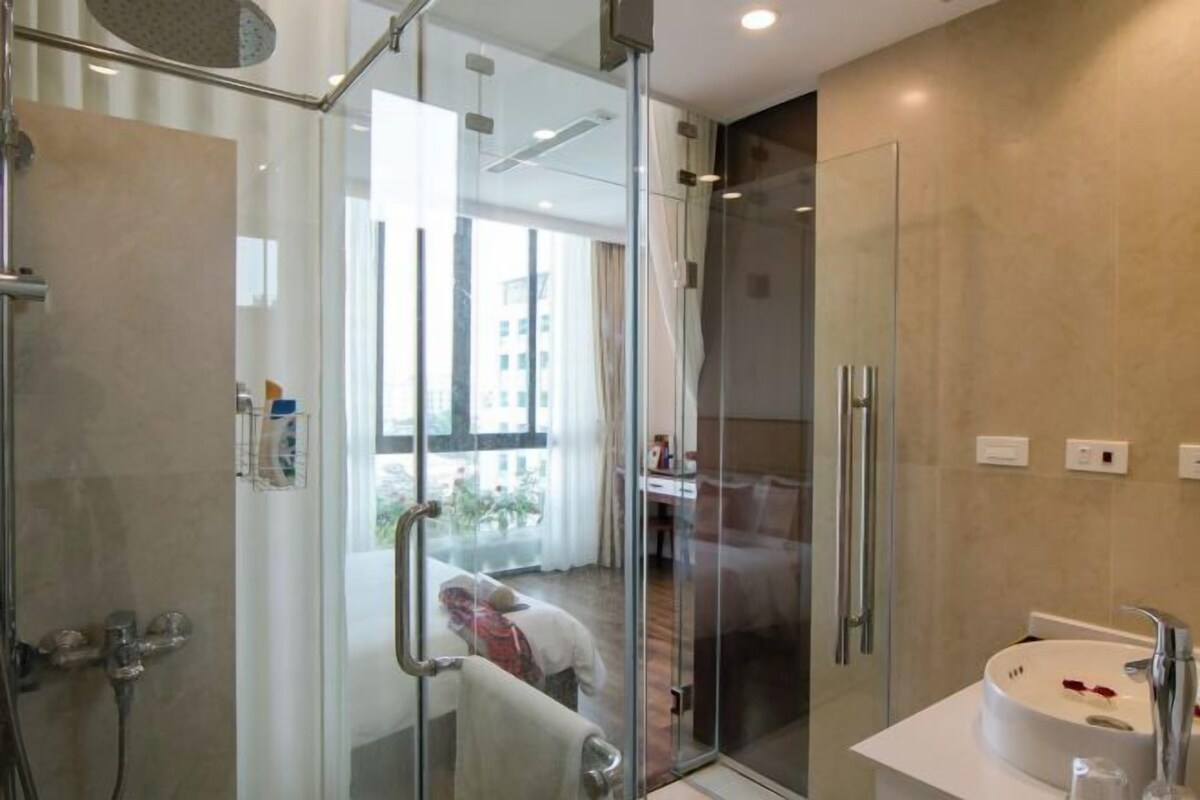 Een moderne badkamer met een douchecabine van glas, een wastafel en uitzicht op een balkon.