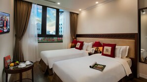 Une chambre d’hôtel avec deux lits, une petite table sur laquelle se trouve un plateau de fruits et des tasses, et une fenêtre avec des rideaux.