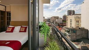 Une chambre d’hôtel avec balcon, un lit avec une literie rouge et une vue sur la ville.