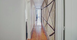 A hallway with wooden flooring, white walls, and a textured wall on the right.