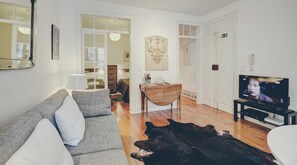 Uma sala de estar com sofá, mesa de madeira, televisão e tapete de couro de vaca.