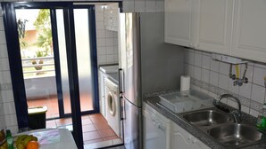 Une cuisine équipée d’un lave-linge, d’un réfrigérateur, d’un évier et d’une fenêtre donnant sur un jardin.