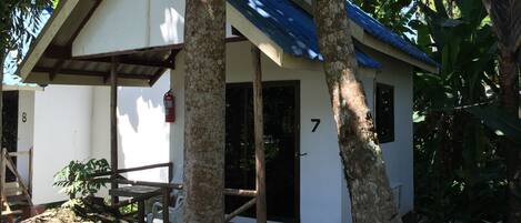 A small, single-story building with a white exterior and blue roof, surrounded by trees.