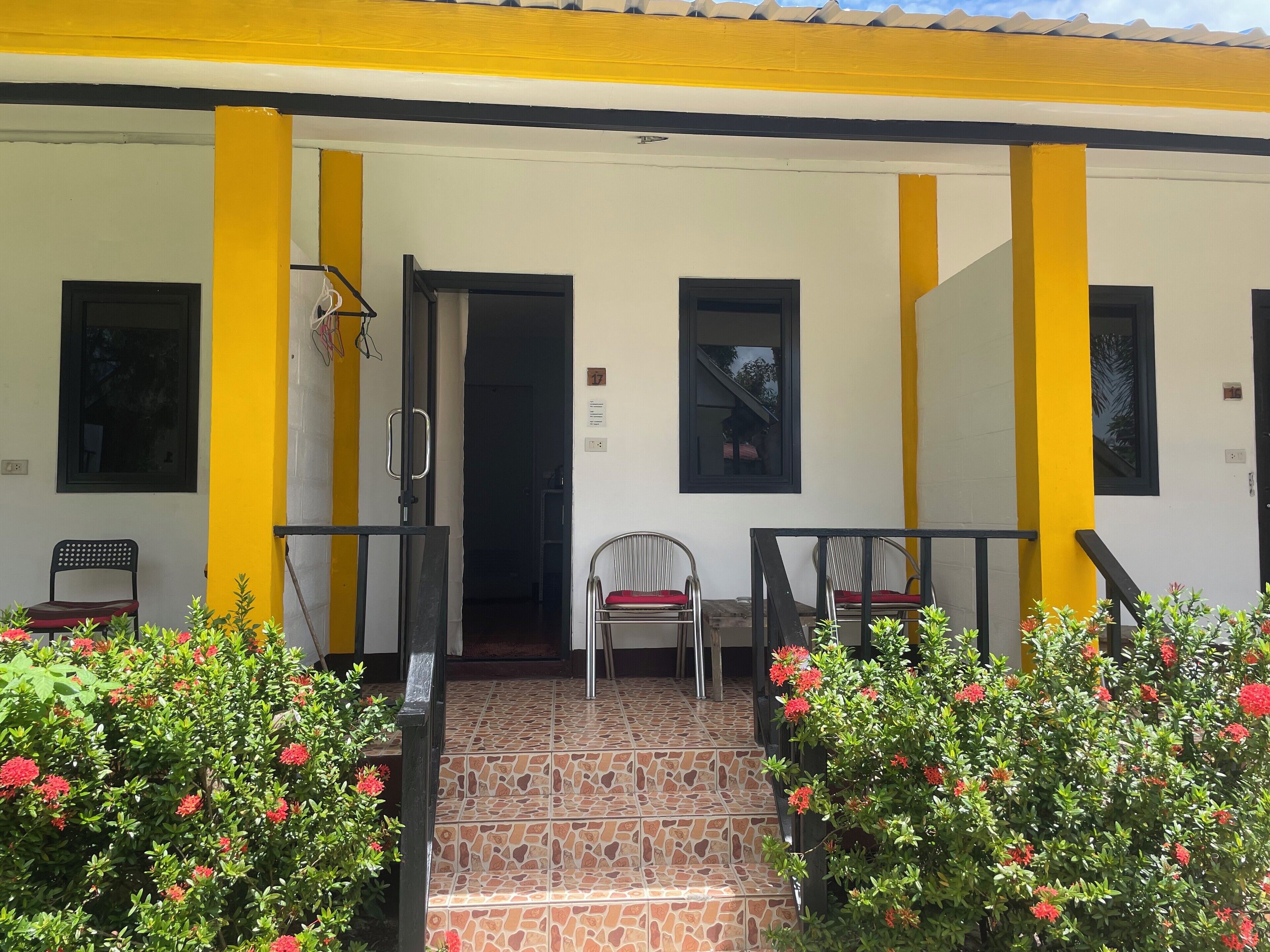 Un edificio con fachada amarilla y blanca, entrada con azulejos y dos sillas afuera.