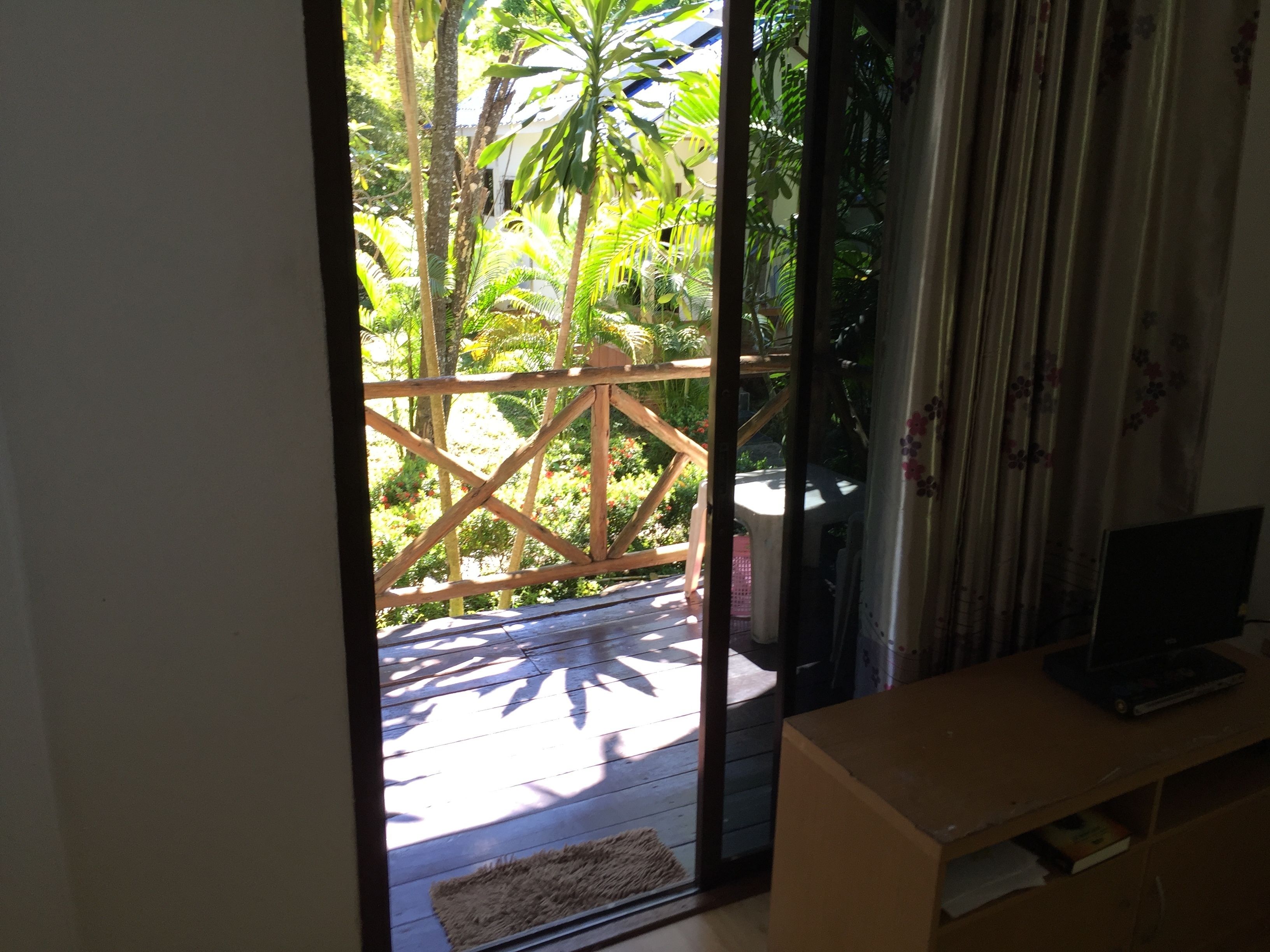 A room with a wooden desk, a television, and a view of a garden through a glass door.
