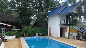 Una piscina con borde de azulejos azules, rodeada por un edificio blanco con techo azul y una escalera que conduce a un balcón.