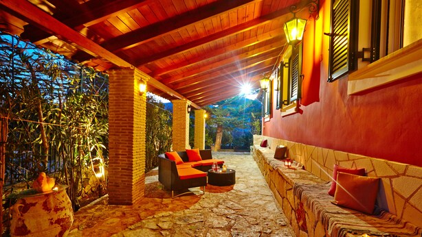 Eine Terrasse im Freien mit Steinböden, einem Korbssessel mit roten Kissen und einer Steinwand mit einer Bank.